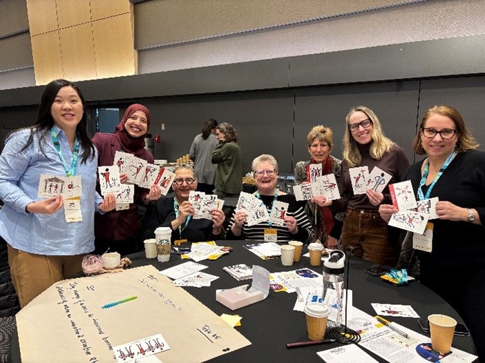 Diverse group of women at a community conference table holding up illustrated cards